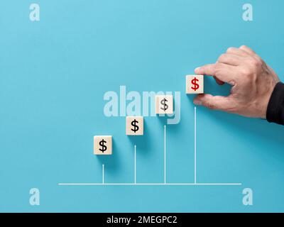 Gewinnsteigerung. Steigerung der Unternehmensinvestitionen oder -Umsätze. Steigender Wohlstand. Männliche Hand ordnet die Holzwürfel mit dem Dollarzeichen auf einem aufsteigenden Diagramm an. Stockfoto