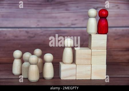 Führungskonzept – zwei Holzfiguren auf Holzblöcken, die anderen nach oben reichen. Führungskonzept. Stockfoto