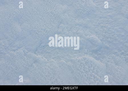 Wunderschöner Winterhintergrund mit schneebedeckten Böden. Natürliche Schneetextur. Windgeformte Muster auf Schneeoberfläche. Stockfoto