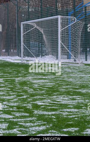 Fußballfeld im Winter, künstliches Gras auf freiem Schnee im Ferntor und Netz. Stockfoto