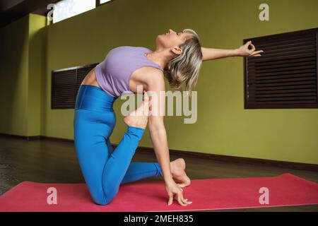 Eine Frau, die einen gesunden Lebensstil führt und Yoga praktiziert, führt eine Variation der Ushtrasana-Übung, Kamelhaltung, allein in Sportbekleidung Sport Stockfoto