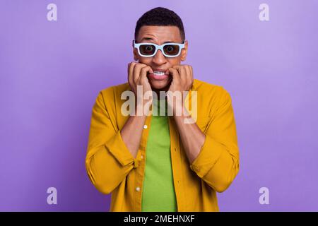 Porträt eines beeindruckten, gutaussehenden Mannes mit gelber Kleidung Brille entsetzt gebissene Finger im Kino isoliert auf violettem Hintergrund Stockfoto