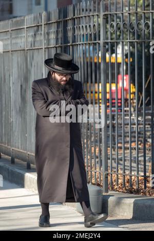 Ein hassidischer Mann ging an einem kalten Wintertag und benutzte seine Mantel-Ärmel als Handschuhe. Keine ungewöhnliche Pose! In Brooklyn, New York. Stockfoto
