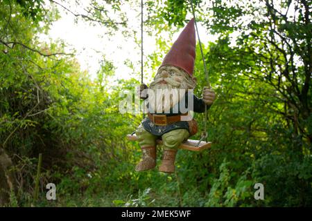 Lustiger Gartenzwerg auf einer Schaukel in einem grünen Garten. Stockfoto