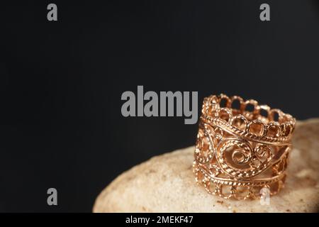 Ein goldener Ring auf einem Stein. Schwarzer Hintergrund mit Kopierbereich. Stockfoto