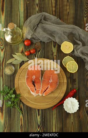 Frisches Lachssteak mit Zutaten auf dunklem Holzhintergrund Stockfoto