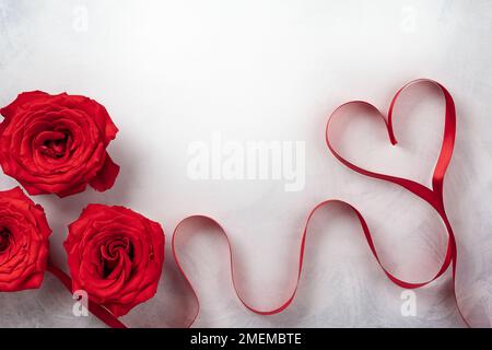 Rote Rosen und rotes Band in Herzform auf klassischem weiß-grauen Hintergrund. Festliches Konzept für den Valentinstag. Draufsicht mit Kopierbereich. Stockfoto
