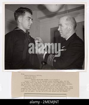 Admiral Schmückt Den Verwundeten Küstenwächter. Foto: George T. Rhodes, 23, aus Awendaw, South Carolina, MM2c, Wer im Pazifik einen Faustkampf mit einem japanischen Seemann hatte, nachdem er einen sinkenden Zerstörer verlassen hatte, erhält das Purple Heart. Konteradmiral Robert Donohue, Chef der Küstenwache, schmückt Rhodos mit der Medaille. Rhodos wurde zweimal durch Schüsse verwundet, bevor sein Schiff abstürzte. Während er vom Schiff wegschwamm, wurde er von einem japanischen Seemann angegriffen, der versuchte, seine Schwimmweste zu holen, aber Rhodes gab dem japanischen Seemann den letzten Schlag und sah ihn nie wieder. Er war einer der CG-Einheiten an Bord der USS Stockfoto