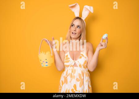 Ein Studio für junge Frauen, isoliert auf Orange, mit Hasenohren und neugierigen Eiern Stockfoto