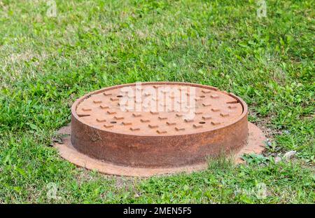 Rostiges Männerloch im Gras. Die Oberseite ist mit quadratischen Unebenheiten bedeckt. Konzentrieren Sie sich auf die nächstgelegene Seite. Platz für Text. Stockfoto