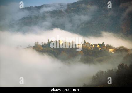Landschaft des nebelverhangenen Dorfes auf einem Hügel, toskanisch-emilianische Apenninen, Italien Stockfoto