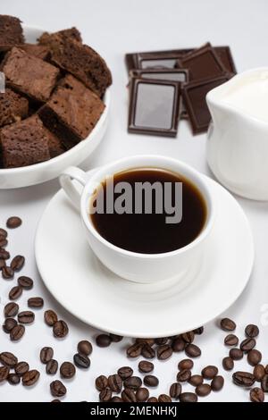 Kaffeekeramantasse mit Milchkanne, Kuchen, Schokolade und Kaffeebohnen auf weißem Hintergrund Stockfoto