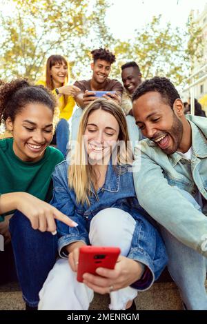 Vertikale Aufnahme von Menschen verschiedener Rassen, die lustige Inhalte auf dem Mobiltelefon ansehen Stockfoto