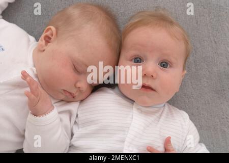 Zwillingsbabys mit Babygros, die auf dem Rücken liegen, Blick von oben, 17 Wochen Stockfoto