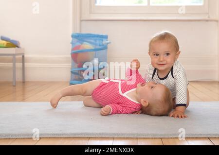 Zwillingsbaby Mädchen und Junge liegen und kriechen auf der Matte, Frontansicht, 10 Monate Stockfoto