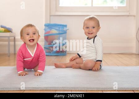 Zwillingsbaby, Mädchen und Junge sitzen und krabbeln auf der Matte, Frontansicht, 10 Monate Stockfoto