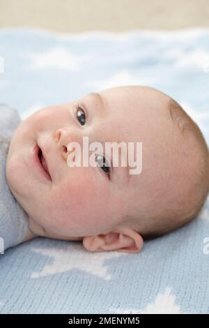 Lächelnder kleiner Junge (16 Wochen), der auf dem Boden auf seinem Rücken lag, Nahaufnahme Stockfoto