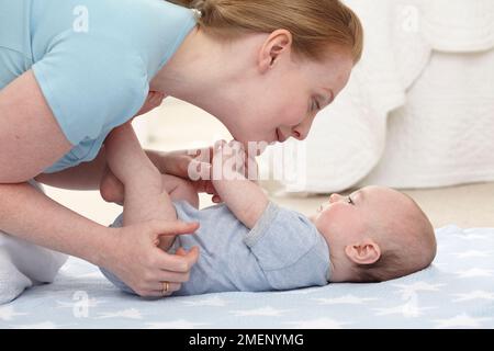 Mutter kniet über dem kleinen Jungen (16 Wochen), der auf dem Boden auf seinem Rücken liegt, Seitenansicht Stockfoto