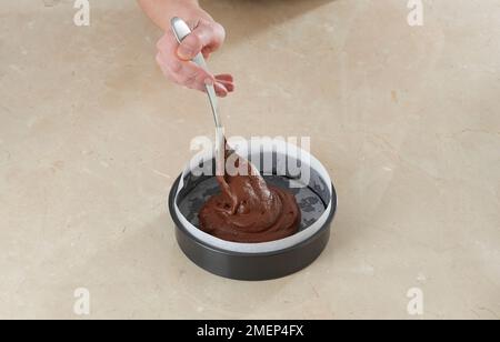 Schokoladen-Fudge-Kuchenbällchen herstellen und die Mischung in eine gefettete und gefütterte Kuchenform gießen Stockfoto