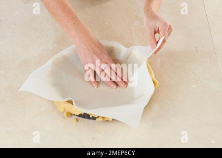 Eine Torte zubereiten, einen Teigkoffer mit Pergament auskleiden, um das blinde Backen vorzubereiten Stockfoto