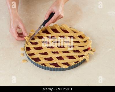 Herstellung von traditioneller österreichischer Torte, Linzertorte, Teigstreifen diagonal über Himbeerfüllung, um Gittermuster zu erzeugen Stockfoto