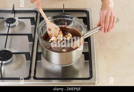 Eine Schokoladentorte zubereiten, Schokolade und Butter in einer Schüssel über einem Topf mit köstlichem Wasser schmelzen lassen Stockfoto