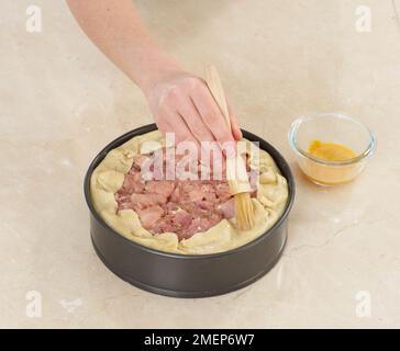 Hähnchen und Schinken, Backkuchen, Kanten mit Eierglasur abbürsten Stockfoto