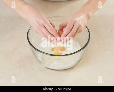 Crepes Suzette zubereiten, Eier zu Milch und Mehlmischung knacken Stockfoto