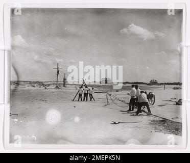 Es wird gezeigt, dass eine Gruppe von Männern an einem Strand arbeitet, die wahrscheinlich an der Entladung von Vorräten oder der Unterstützung militärischer Operationen beteiligt sind. Das Bild zeigt die Routineaufgaben bei Strandlandungen während des Krieges. Stockfoto