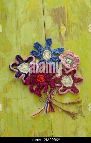 Bunte Strickblumen auf grünem Holzhintergrund Stockfoto