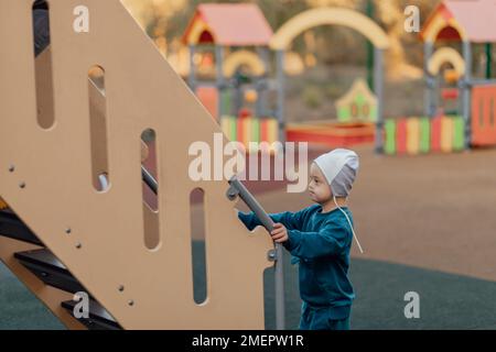 Ein kleiner Junge mit Down-Syndrom klettert die Treppe hoch, um zu rutschen Stockfoto