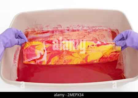 Halten Sie zwei Ecken des Stoffes schnell nach oben, damit überschüssiges Wasser und marmorierende Tinte abtropfen können, Nahaufnahmen Stockfoto