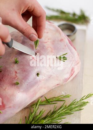 Die Schenkel des Lammes mit Rosmarin stopfen und mit Hilfe der Messerspitze die Splinte in die Löcher stecken Stockfoto