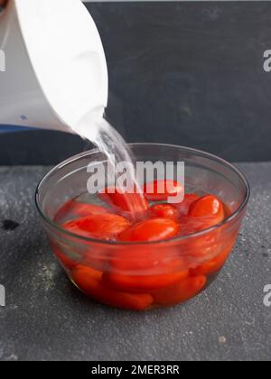 Gießen Sie in einer hitzebeständigen Schüssel kochendes heißes Wasser über Tomaten Stockfoto