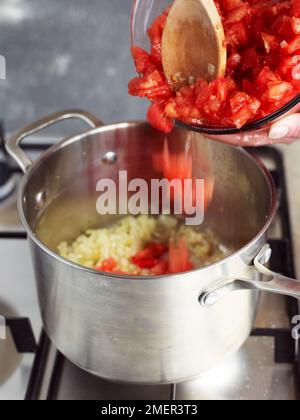 Zugabe gehackter Tomaten in den Topf mit Zwiebeln (Kochen von Tomatensoße) Stockfoto