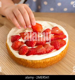 Auflegen von Erdbeerscheiben auf cremefarbenen Schwammkuchen Stockfoto