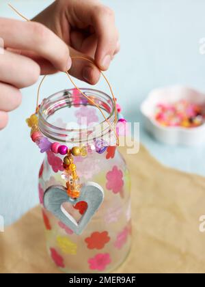 Gläser aus Kerzenglas mit Papiertaschenblumen, silberner Pendelleuchte und Perlen Stockfoto