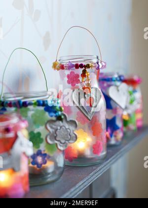 Gläser aus Kerzenglas mit Papiertaschenblumen und silbernen Anhängern auf dem Kaminsims Stockfoto