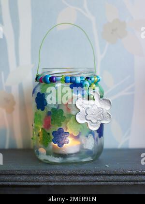 Gläser aus Kerzenglas mit Papiertaschenblumen und silbernen Anhängern auf dem Kaminsims Stockfoto