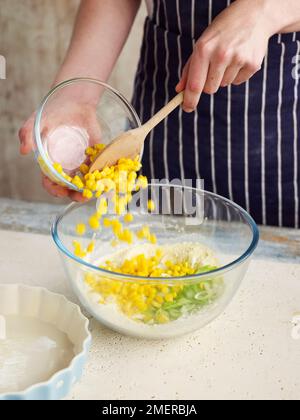 Maisbrot, der Mais in eine große Schüssel mit Mehl und gehackten Frühlingszwiebeln gießt Stockfoto