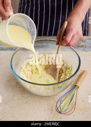 Maisbrot, Ei- und Milchmischung in eine Schüssel mit Mais, Frühlingszwiebeln und Mehl Stockfoto