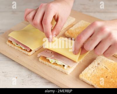 Club Sandwich, dazu Scheiben Schinken und Käse auf getoastetes Weißbrot Stockfoto