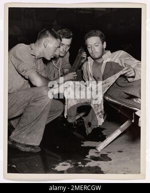 Die Küstenwache bringt die Verwundeten raus. Ein Kollege des Apothekers, an Bord einer von der Küstenwache bemannten LST irgendwo in der Pacific Invasion Zone, Marine Corp John T. Curry (rechts) aus Decatur, Illinois, wurde bei einem Strandangriff verwundet und stellt zwei Küstenwachmännern, die im schwimmenden Krankenhaus Dienst hatten, eine von Kugeln durchlöcherte japanische Kampfflagge aus. Es sind David Green (Vordergrund), der Freund des Apothekers zweiter Klasse, aus Staten Island, New York, und Shelby K. Lay, Bootsmann zweiter Klasse, aus Harrison, Arkansas. Stockfoto