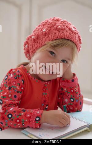 Mädchen mit gestrickter Beanie-Mütze, die Bilder in einem Notizbuch malt, 3,5 Jahre Stockfoto