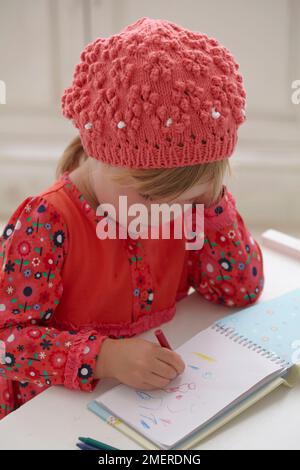 Mädchen mit gestrickter Beanie-Mütze, die Bilder in einem Notizbuch malt, 3,5 Jahre Stockfoto