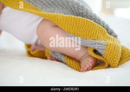 Ein kleines Mädchen, das auf dem Bett krabbelt, eine gestrickte Kapuzendecke trägt, 9 Monate Stockfoto