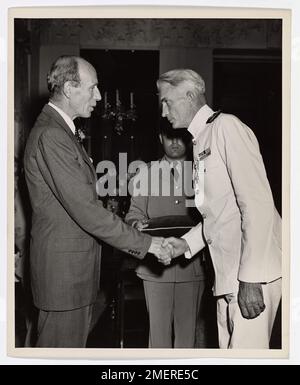 Dank einem Offizier der britischen Küstenwache. Mit einem höflichen Bogen für die Königsfamilie, Lieutenant Commander Louis I. der Küstenwache Reilly aus Port Richmond, Staten Island, New York, nimmt die Glückwünsche des Earl of Halifax, britischer Botschafter, entgegen, nachdem er das Britische Dienstkreuz bei der britischen Botschaft in Washington, D.C. empfangen hat Der Veteran der Küstenwache eines Vierteljahrhunderts-Dienstes gewann die zweithöchste britische Kampfmedaille für "Tapferkeit, Geschick und unbeirrte Pflichtbereitschaft", indem er eine LST-Gruppe befehligte, die die berühmte britische Siebte Panzerdivision landete - die "Wüstenratten" Stockfoto