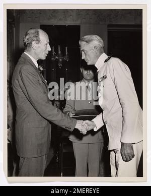 Dank Einem Offizier der britischen Küstenwache. Mit einem höflichen Bogen für die Königsfamilie, Lieutenant Commander Louis I. der Küstenwache Reilly aus Port Richmond, Staten Island, New York, nimmt die Glückwünsche des Earl of Halifax, britischer Botschafter, entgegen, nachdem er das Britische Dienstkreuz bei der britischen Botschaft in Washington, D.C. empfangen hat Der Veteran der Küstenwache eines Vierteljahrhunderts-Dienstes gewann die zweithöchste britische Kampfmedaille für "Tapferkeit, Geschick und unbeirrte Pflichtbereitschaft", indem er eine LST-Gruppe befehligte, die die berühmte britische Siebte Panzerdivision landete - die "Wüstenratten" Stockfoto