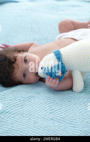 Baby, das auf dem Bett lag und einen gestrickten Eisbären hielt, 4,5 Monate Stockfoto
