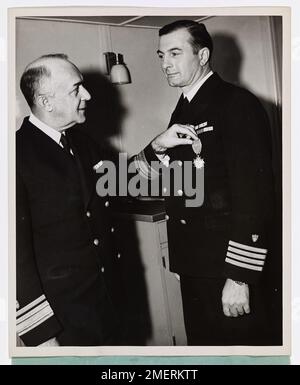 RADM Leon C. Covell überreicht Captain Edward H. Fritzsche der Küstenwache mit der Legion of Merit Medaille. Captain Edward H. Fritzsche (rechts), Kapitän eines von der Küstenwache bemannten Invasionstransports, erhält am D-Day bei der Invasion in der Normandie die Legion of Merit Medaille für „außergewöhnlich verdienstvolles Verhalten“ als Befehlshaber der Angriffsgruppe amerikanischer und britischer Transporte und Landefahrzeuge. Konteradmiral Leon C. Covell wird bei der Präsentation gezeigt. Hauptmann Fritzsche leitete die Entladung der berühmten "Fighting First Division", die eine Verwarnung der Präsidenteneinheit erhielt. Hauptmann Fr Stockfoto